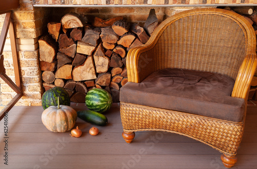 Wicker chair sits on veranda. Nearby vegetables and firewood..