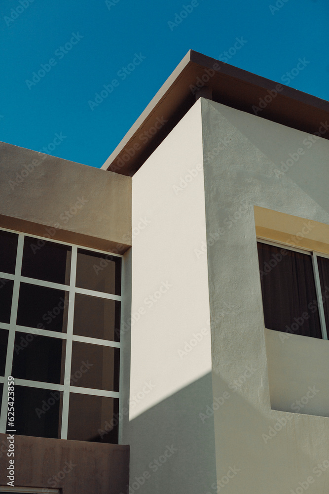 Light casts shadows on a minimalist building against a blue sky. Light casts shadows on a minimalist building against a blue sky.