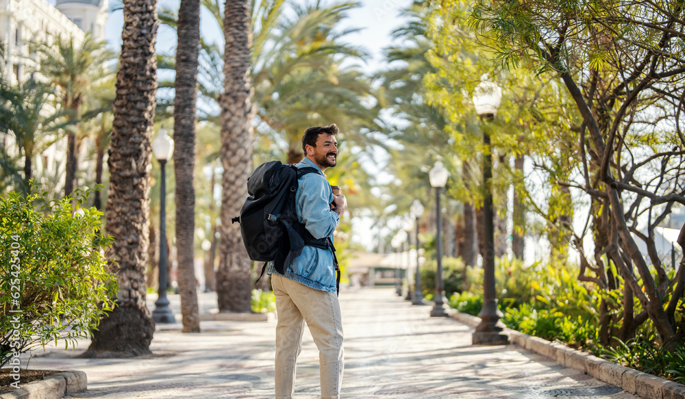 A traveler with backpack is walking on the tropical street during his vacation in Spain.