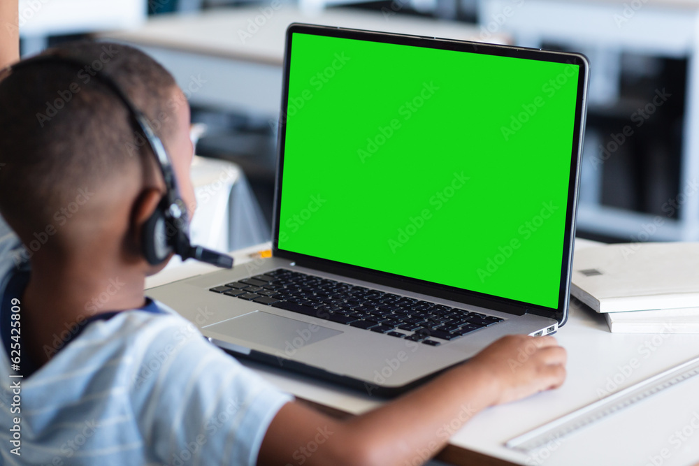 African american boy wearing headphones and studying online over laptop on table at home African american boy wearing headphones and studying online over laptop on table at home
