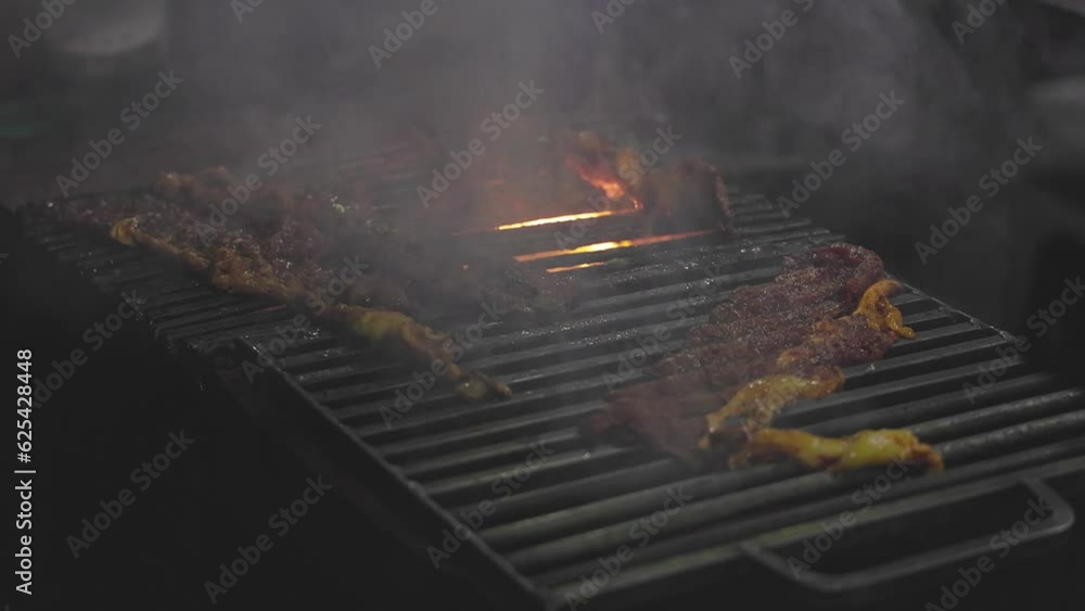 Closeup of a man grilling marinated raw meat or beef slices on a charcoal grill Closeup of a man grilling marinated raw meat or beef slices on a charcoal grill