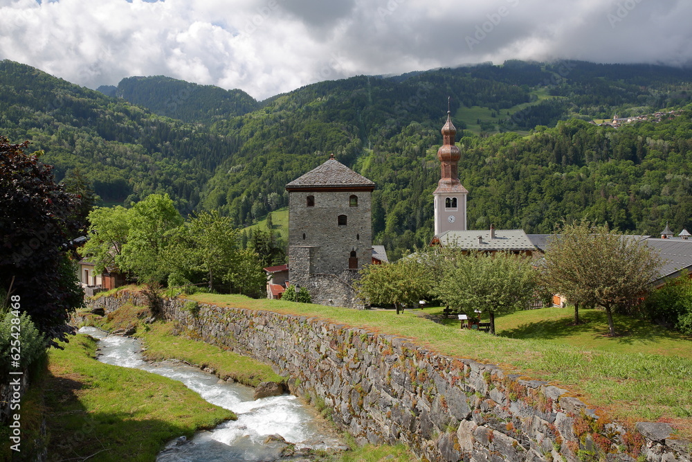The church of Saint Francois de Sales and the Tour de Bozel (Bozel tower), located in the commune Bozel, Northern French Alps, Tarentaise, Savoie, France, with the mountain stream Le Bonrieu  
