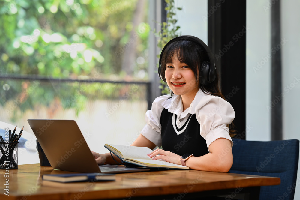 Online education, e-learning. Happy Asian young woman wearing headphone, studying remotely, using a laptop Online education, e-learning. Happy Asian young woman wearing headphone, studying remotely, using a laptop