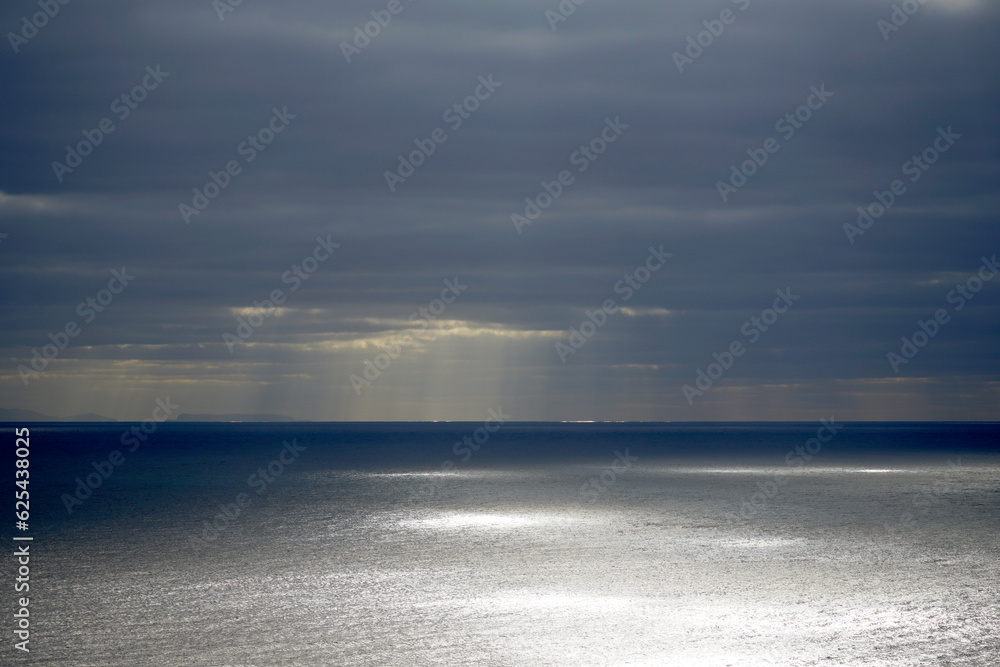 Morning and clouds over the Atlantic Ocean. Bright sunlight and glare on the water. Dark rainy sky