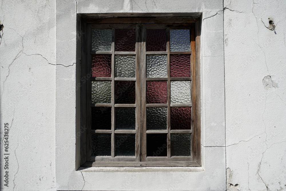 Window to the house with stained-glass windows. Cracked white plaster