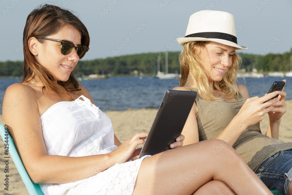 mother and daughter reading book and e-book on sea shore