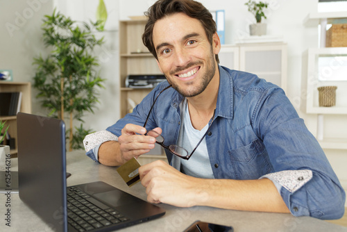 Foto smiling man using card to make online purchase on laptop