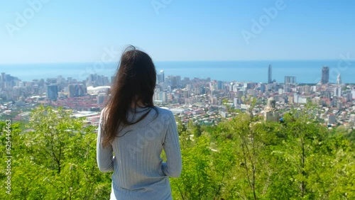 Woman tourist admiring cityscape of coastal Batumi city and sea from mountain in Georgia. Travel tourism, wanderlust, adventure, explore, visiting places of interest, attractions, sights concept. photo