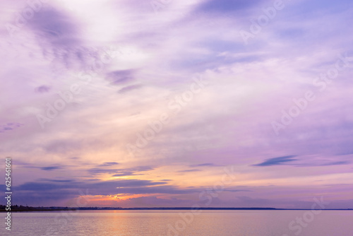 Colorful sky background on sunset or sunrise, purple pastel color clouds and surface water on lake. Aesthetic view nature abstract cloudscape, natural blue pink purple shades and skyline water