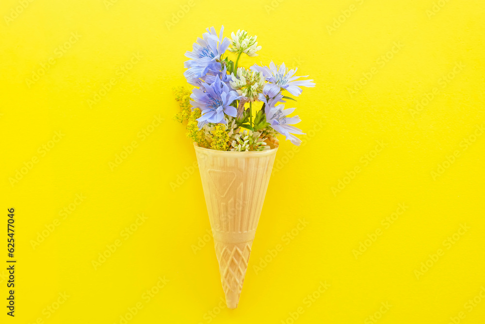 Chicory flowers and other wild flowers in an ice cream cone on a yellow background. Flat top view.