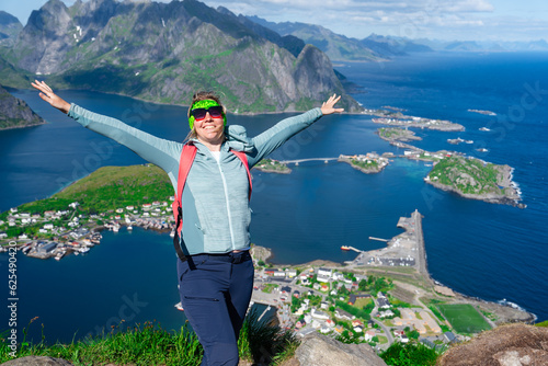Happy woman hiker enjoys the panorama of lofoten islands at the top of Reinebringen. traveler alone on cliff edge in Norway lifestyle exploring concept. Hike above Reine village in the Lofoten photo