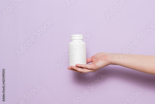 White plastic bottle in female hand. Packaging for pills  capsules or supplements.