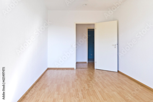 Empty room with white walls and wood laminate flooring, door open to the hallway. New home concept background texture with lots of text or copy space.