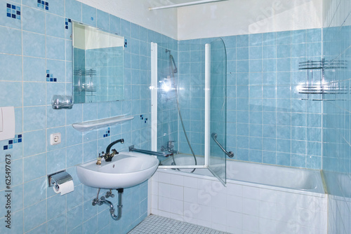 Unrenovated bathroom from the 1970s with the original blue tiles, seventies style. Outdated, neglected and grimy bath in an apartment for rent. photo