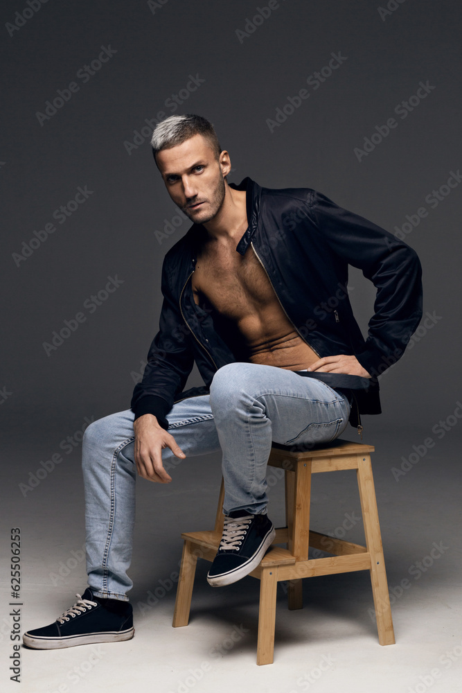 A young guy with gray hair in a black jacket and blue jeans poses on a gray background A young guy with gray hair in a black jacket and blue jeans poses on a gray background