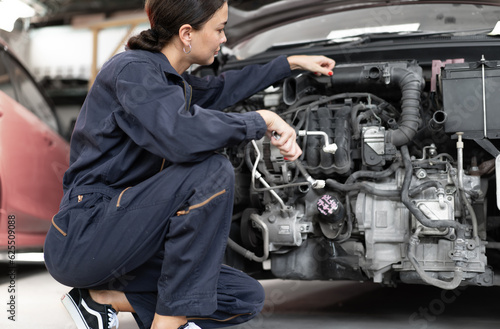 Female auto mechanic hold wrench diagnose broken engine car repairing in mechanics garage. Engineer inspecting motor part problems. Woman empowerment working in automotive maintenance service industry