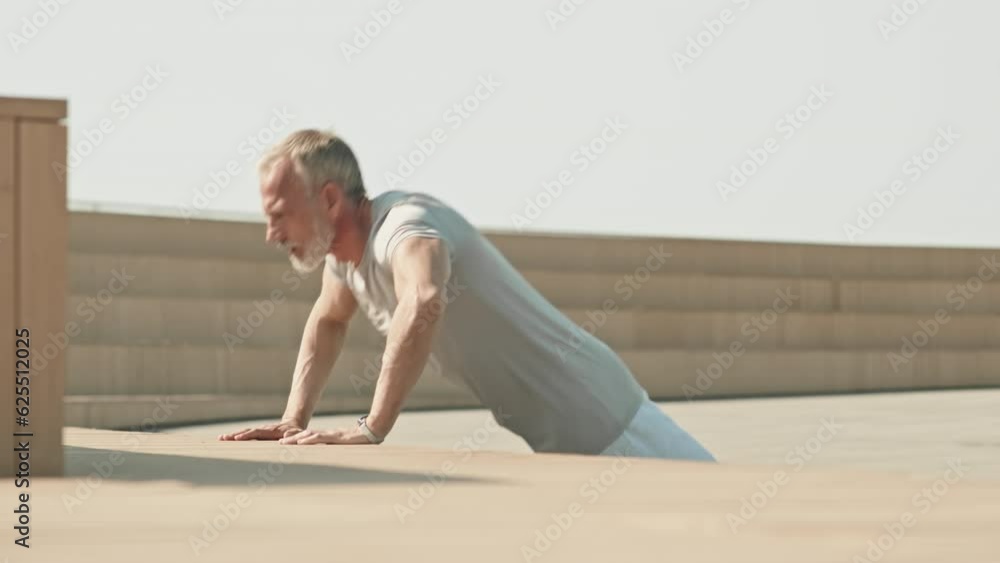 Muscular senior man in sportswear practicing push ups at urban public space while working out outdoors in morning Muscular senior man in sportswear practicing push ups at urban public space while working out outdoors in morning