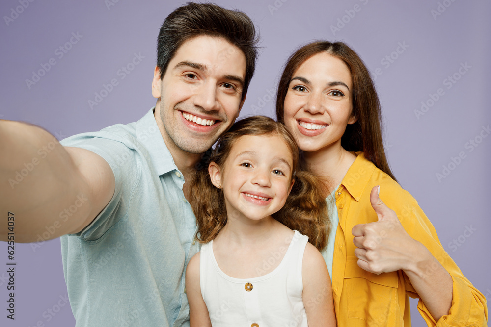 Close up young fun happy parents mom dad with child kid daughter girl 6 year old wear blue yellow casual clothes do selfie shot pov mobile cell phone show thumb up isolated on plain purple background. Close up young fun happy parents mom dad with child kid daughter girl 6 year old wear blue yellow casual clothes do selfie shot pov mobile cell phone show thumb up isolated on plain purple background.