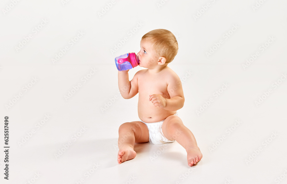 Cute, adorable baby, toddler in diaper sitting and eating, drinking water from bottle against white studio background. Concept of childhood, newborn lifestyle, happiness, care. Copy space for ad Cute, adorable baby, toddler in diaper sitting and eating, drinking water from bottle against white studio background. Concept of childhood, newborn lifestyle, happiness, care. Copy space for ad