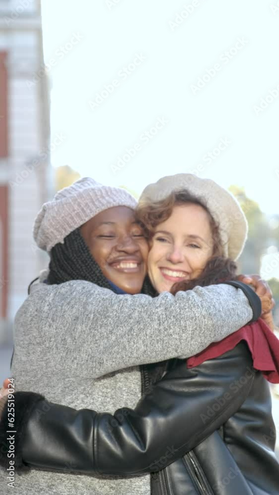 Two multiracial female happy friends hugging each other and smiling on city street. Two multiracial female happy friends hugging each other and smiling on city street.
