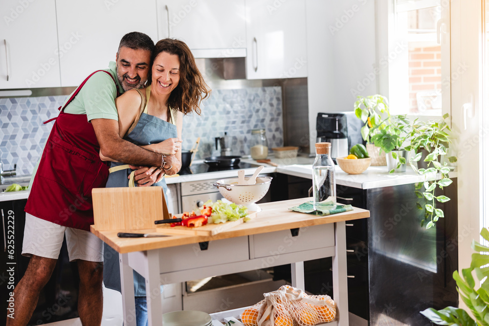 happy mature couple, they are hugging happily while cooking and watching a recipe video on digital tablet happy mature couple, they are hugging happily while cooking and watching a recipe video on digital tablet