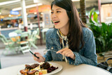 Asian Japanese woman is happy to chat with friends while eating grilled steak meal outdoors. Women enjoy having food with laughing.