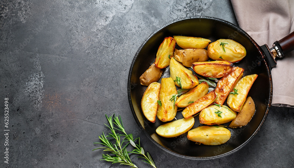 Roasted potatoes. Baked potato wedges in frying pan on dark stone background. Top view with copy space. Roasted potatoes. Baked potato wedges in frying pan on dark stone background. Top view with copy space.