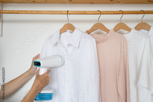 An unrecognizable woman steams a shirt hanging on a wooden hanger