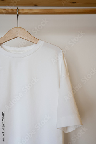 White t-shirt hanging on wooden hanger in wardrobe, closeup