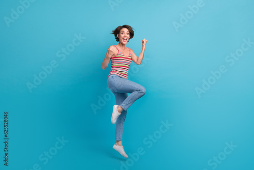 Fototapeta Naklejka Na Ścianę i Meble -  Full body photo of delighted cheerful lady jumping raise fists triumph luck isolated on blue color background