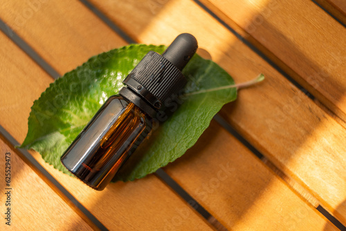 A bottle of essential oils on a green leaf. The background is made of natural wood. place to copy. Natural cosmetics for skin and health care