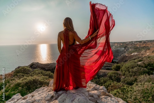 Woman sunset sea red dress  back view a happy beautiful sensual woman in a red long dress posing on a rock high above the sea on sunset.