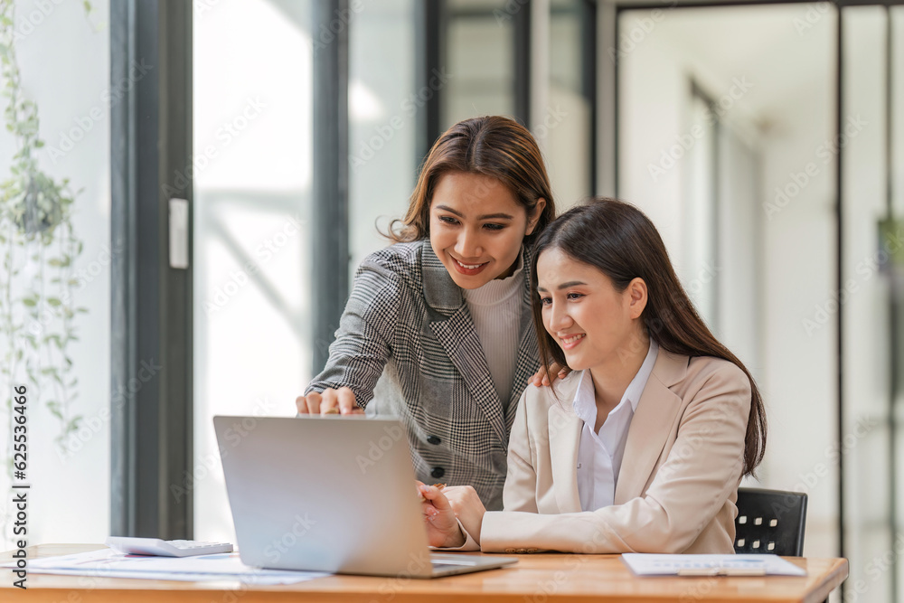 Two happy professional coworkers discussing plan at work. explaining Asian colleague financial project on laptop in office Two happy professional coworkers discussing plan at work. explaining Asian colleague financial project on laptop in office