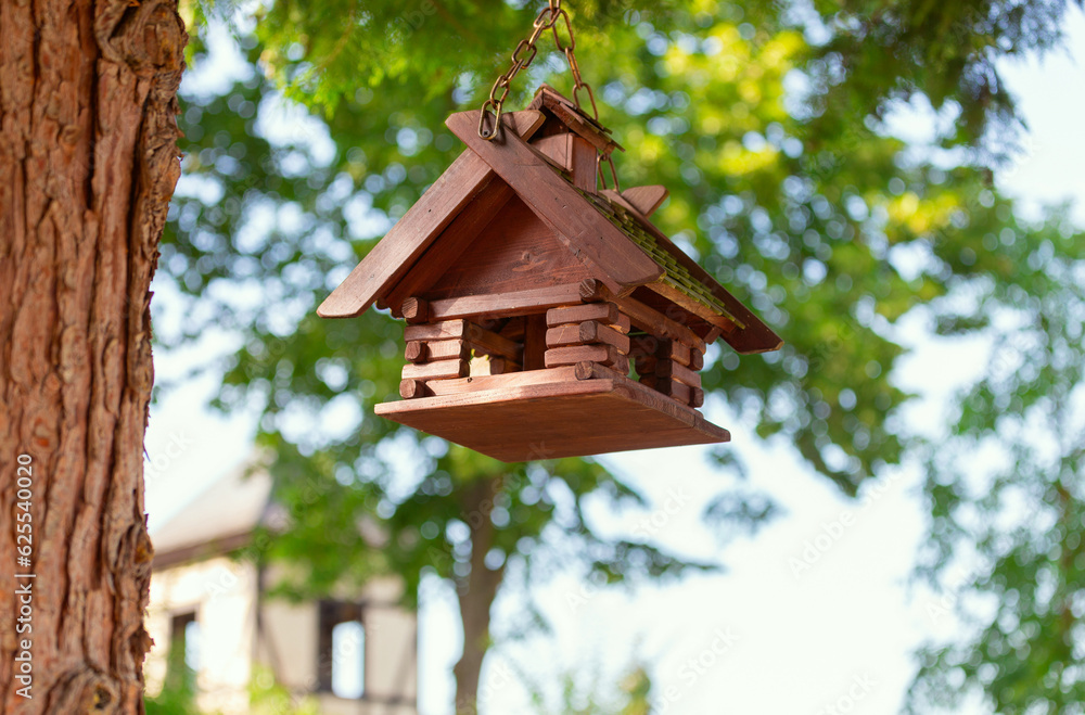 A wooden birdhouse suspended from a pine tree. A wooden birdhouse suspended from a pine tree.