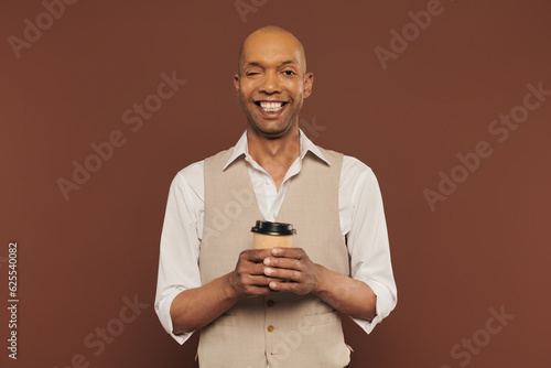 inclusion, happy and bold african american man with myasthenia gravis syndrome, standing with paper cup, dark skinned man with chronic disease on brown background, coffee to go