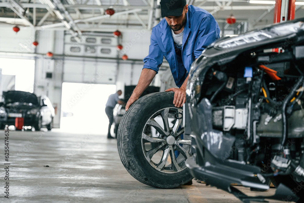 New tire, moving it. Auto mechanic working in garage. Repair service