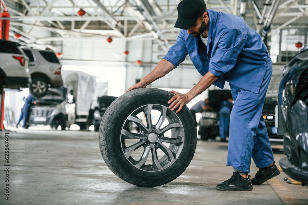 New tire, moving it. Auto mechanic working in garage. Repair service New tire, moving it. Auto mechanic working in garage. Repair service
