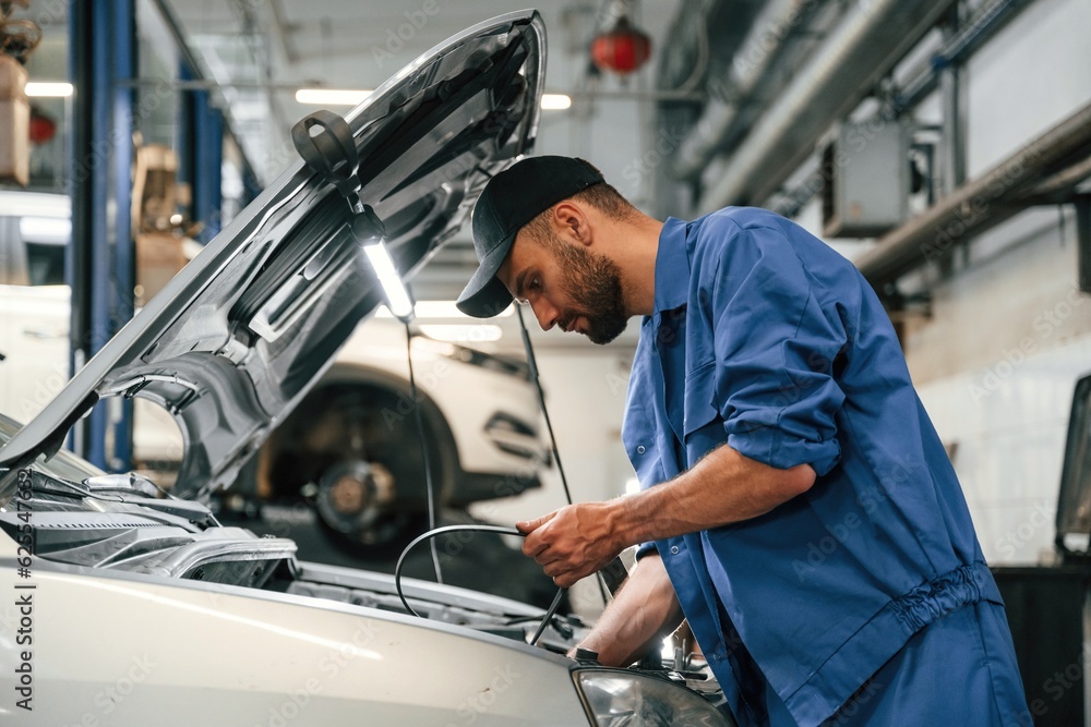 Adjusts the cable. Auto mechanic working in garage. Repair service Adjusts the cable. Auto mechanic working in garage. Repair service