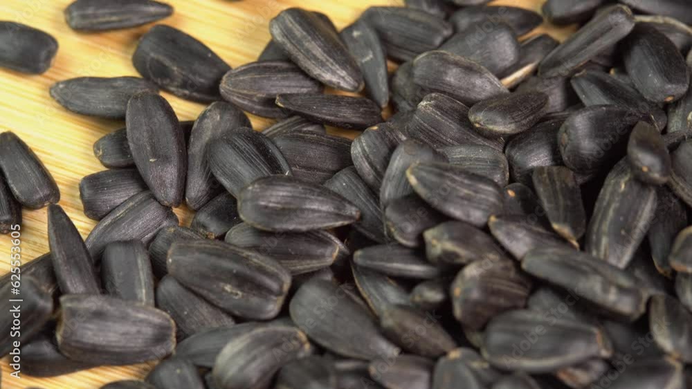 Roasted Sunflower Seeds Close-up Pouring on table. Harvesting Sunflower Unpeeled Seeds, Healthy Source of Vitamins in Vegan Food. Raw Materials for Sunflower Oil Roasted Sunflower Seeds Close-up Pouring on table. Harvesting Sunflower Unpeeled Seeds, Healthy Source of Vitamins in Vegan Food. Raw Materials for Sunflower Oil