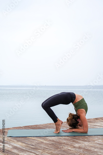 Woman practicing yoga by the sea on a deck - Urdhva dhanurasana - Wheel pose