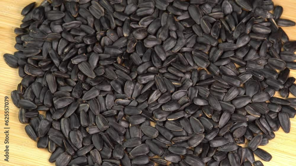Roasted Sunflower Seeds Close-up rotate on wooden background. Harvesting Sunflower Unpeeled Seeds, Healthy Source of Vitamins in Vegan Food. Raw Materials for Sunflower Oil Roasted Sunflower Seeds Close-up rotate on wooden background. Harvesting Sunflower Unpeeled Seeds, Healthy Source of Vitamins in Vegan Food. Raw Materials for Sunflower Oil