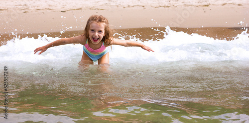 Beautiful happy little girl playing in the waves and splashes on the sea