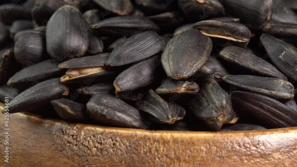 Roasted Sunflower Seeds Close-up Rotate in wooden bowl on black background. Harvesting Sunflower Unpeeled Seeds, Healthy Source of Vitamins in Vegan Food. Raw Materials for Sunflower Oil Roasted Sunflower Seeds Close-up Rotate in wooden bowl on black background. Harvesting Sunflower Unpeeled Seeds, Healthy Source of Vitamins in Vegan Food. Raw Materials for Sunflower Oil