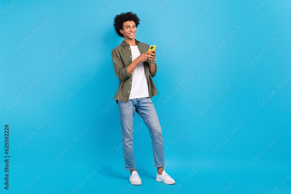 Full size portrait of positive young person hold use smart phone chatting isolated on blue color background Full size portrait of positive young person hold use smart phone chatting isolated on blue color background