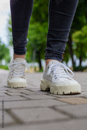 White sneakers with studded soles on female legs in black jeans