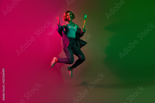 Full length photo of crazy excited lady jumping winning web lottery eshopping isolated on colorful vivid neon background © deagreez