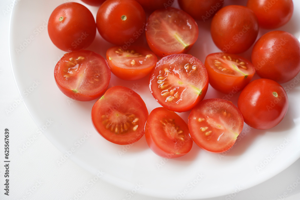 Fresh red fruits of small tomatoes on a glass plate. Juicy chopped cherry tomatoes. Fresh red fruits of small tomatoes on a glass plate. Juicy chopped cherry tomatoes.