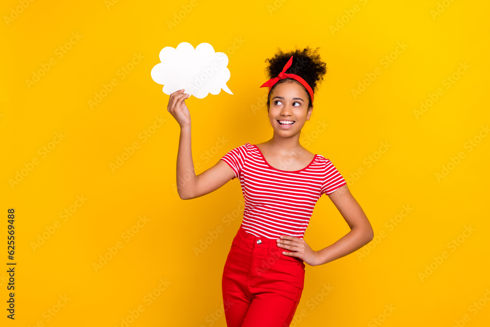 Portrait of little cheerful schoolgirl look hand hold empty space paper cloud shape bubble card isolated on yellow color background Portrait of little cheerful schoolgirl look hand hold empty space paper cloud shape bubble card isolated on yellow color background