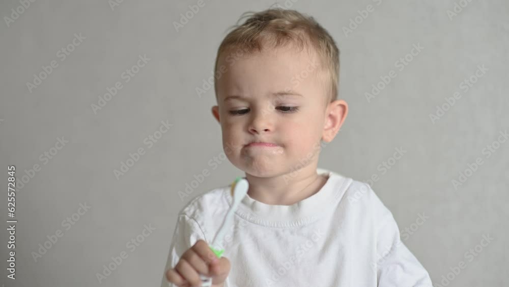 the kid is brushing his teeth with a toothbrush on a gray background. Oral hygiene. the kid is brushing his teeth with a toothbrush on a gray background. Oral hygiene.