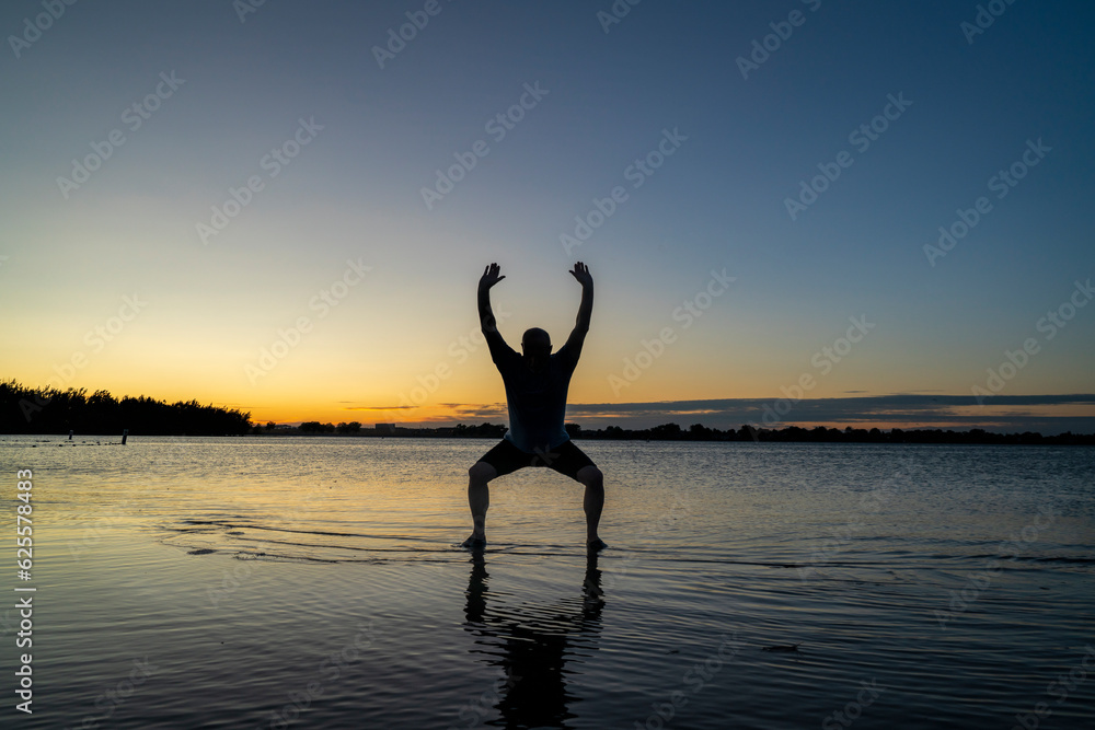 sunrise silhouette of a man standing in shallow water and practicing chigong or tai chi movements, Boyd Lake State Park in northern Colorado